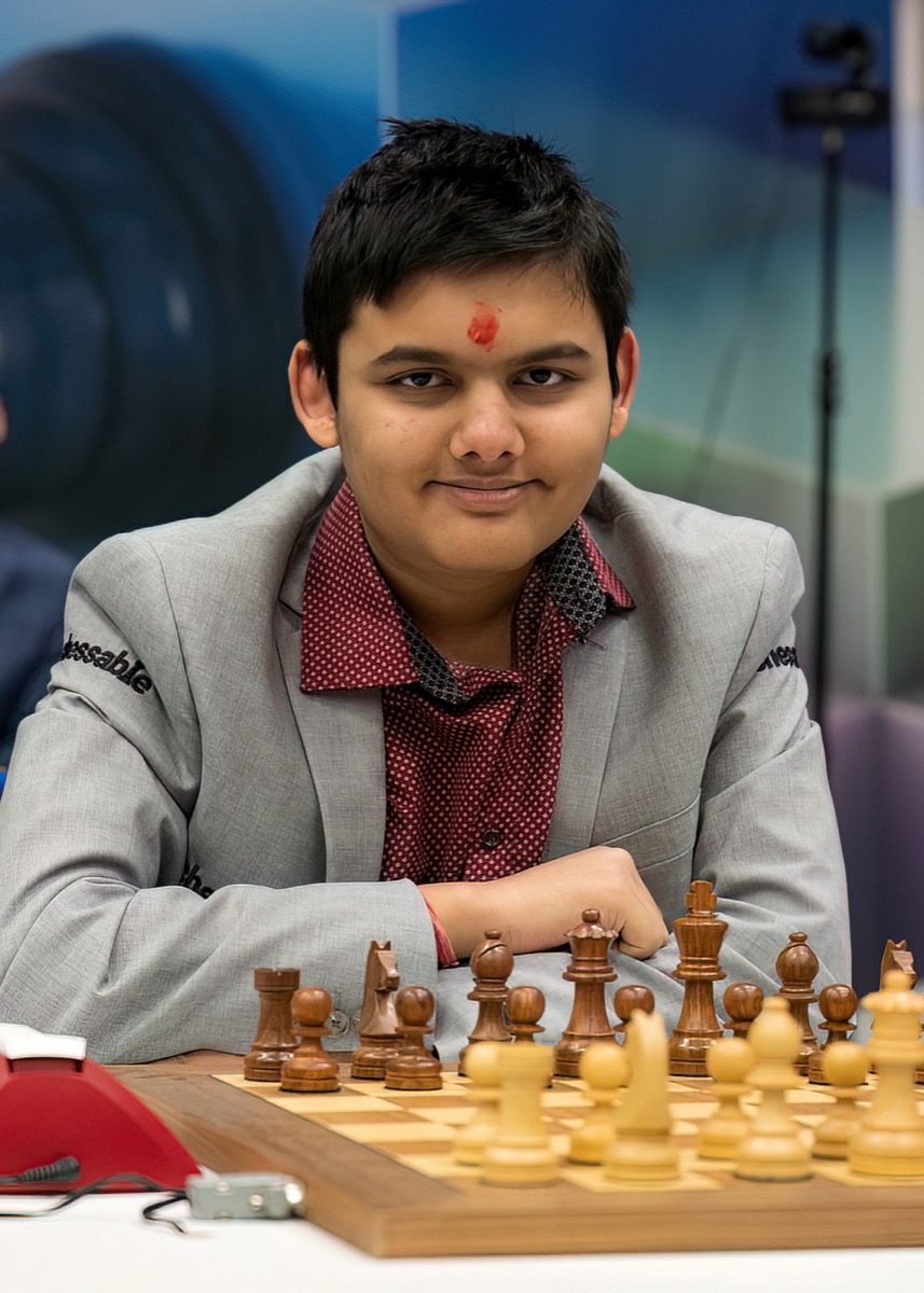 Abhimanyu Mishra seated at the board at the 2023 Tata Steel Chess Tournament, arms folded on the table, in a grey jacket
