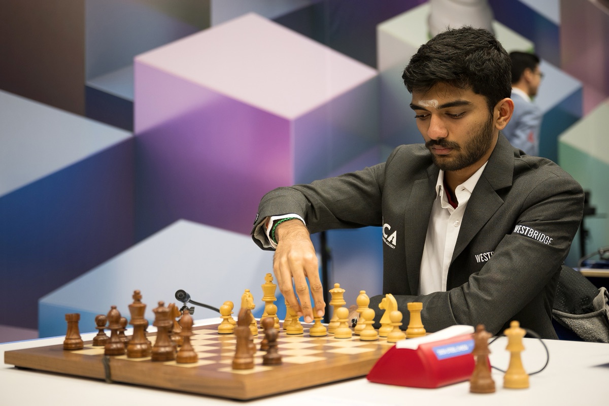 Gukesh Dommaraju at the board in a dark suit, reaching to move a white pawn, at the 2025 Tata Steel Chess Tournament